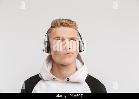 Portrait Nahaufnahme des nachdenklichen jungen Mann 16-18 Jahre alt looking beiseite und verdrehen Mund, während Sie Musik hören über kabellose Kopfhörer isoliert ov Stockfoto