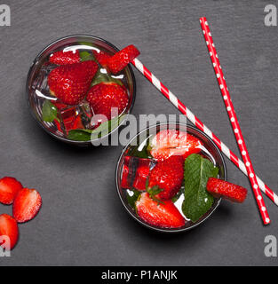 Sommer kaltes Getränk mit Erdbeeren, Minze und Eis im Glas auf schwarzem Hintergrund. Nahaufnahme des Cocktails mit frischen Früchten. Stockfoto