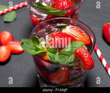 Sommer kaltes Getränk mit Erdbeeren, Minze und Eis im Glas auf schwarzem Hintergrund. Nahaufnahme des Cocktails mit frischen Früchten. Stockfoto