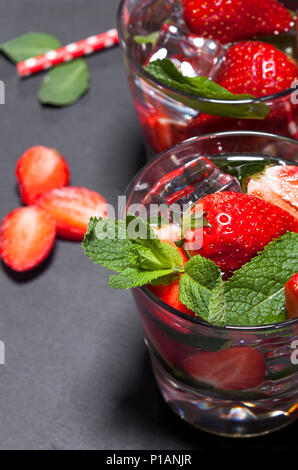 Sommer kaltes Getränk mit Erdbeeren, Minze und Eis im Glas auf schwarzem Hintergrund. Nahaufnahme des Cocktails mit frischen Früchten. Stockfoto