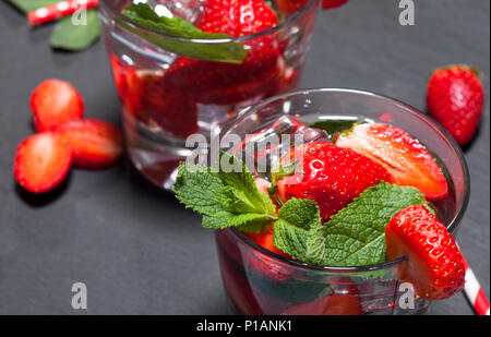 Sommer kaltes Getränk mit Erdbeeren, Minze und Eis im Glas auf schwarzem Hintergrund. Nahaufnahme des Cocktails mit frischen Früchten. Stockfoto