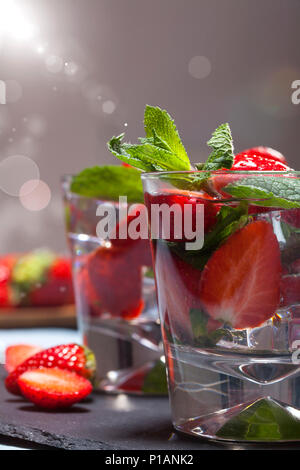 Sommer kaltes Getränk mit Erdbeeren, Minze und Eis im Glas auf schwarzem Hintergrund. Nahaufnahme des Cocktails mit frischen Früchten. Stockfoto