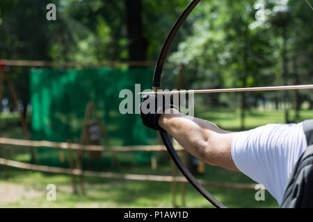 Archer Hände mit Holz- Bogen schießen Pfeil. Bogenschießen Turnier im Wald. Bowman vor den Dreharbeiten von einem langbogen. Close Up, selektiver Fokus Stockfoto