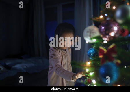 Neugierig, süße Mädchen berühren beleuchtete Weihnachtsbaum Stockfoto