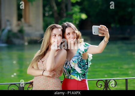 Zwei Mädchen nehmen eine selfie zusammen und Lächeln. Im Hintergrund Der Grüne See im Park. Stockfoto