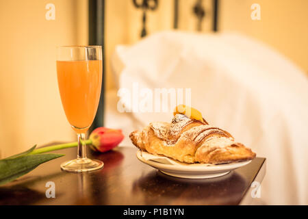 Süßes Frühstück im Hotel Zimmer. Croissant mit gelb Creme, Glas Orangensaft und Blume auf dem Tisch Stockfoto