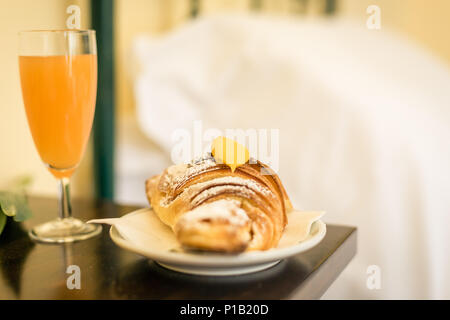 Süßes Frühstück im Hotel Zimmer. Croissant mit gelb Creme, Glas Orangensaft und Blume auf dem Tisch Stockfoto