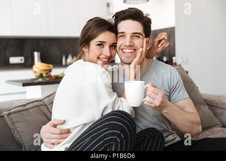 Porträt einer reizenden jungen Paar Kaffee trinken, beim Sitzen auf der Couch und küssen Stockfoto