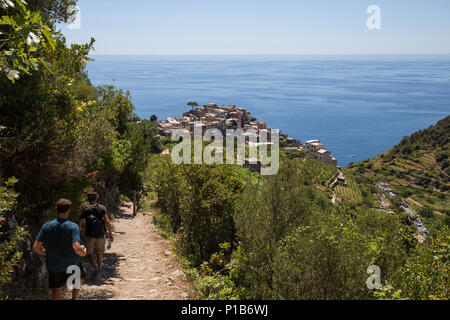 Blick auf Corniglia Dorf aus dem Pfad auf dem Hügel und zwei Reisende. Cinque Terre, Ligurien, Italien Stockfoto