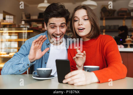 Glückliches junges Paar sitzen an einem Tisch zusammen und Cafe in einer Videokonferenz Stockfoto