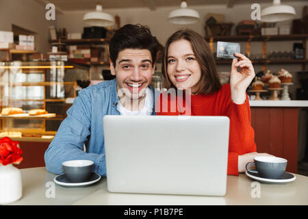 Glückliches junges Paar mit Kreditkarte und Sitzen im Cafe Tabelle mit Laptop Stockfoto