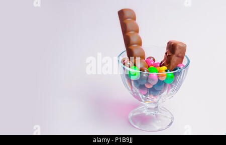 Süßigkeiten in einem Glas Vase auf einem rosa Hintergrund, Schokoriegel, bunte Bonbons Stockfoto