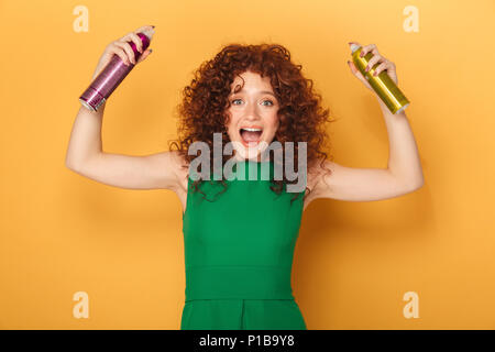 Portrait einer aufgeregt Curly rothaarige Frau mit zwei haarsprays auf gelben Hintergrund isoliert Stockfoto