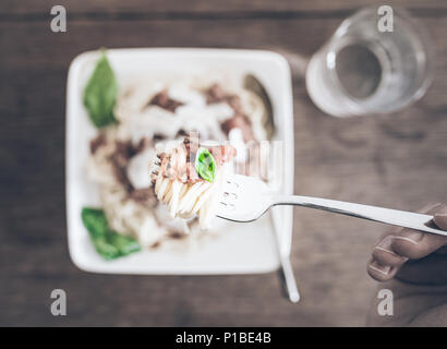 POV-shot der Person essen Nudeln mit Bolognese Sauce gegen rustikalen Holztisch Stockfoto