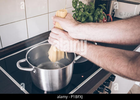 Hände, Spaghetti in den Topf mit kochendem Wasser Herd Stockfoto
