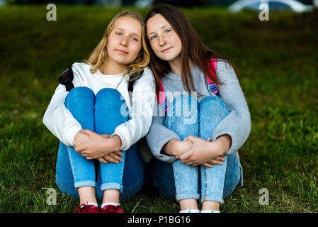 Zwei Mädchen im Teenageralter. Sommer in der Natur. Sie sitzen auf Gras. Miteinander kommunizieren. Auf der Kamera dar. Die besten Freunde. Datenschutz Die von den Erwachsenen. Stockfoto