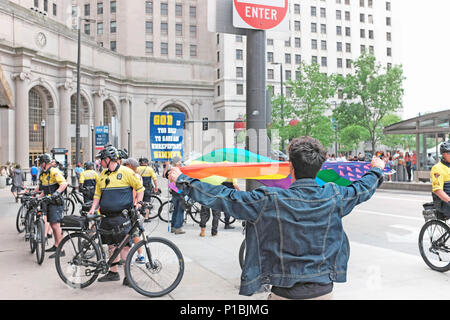 Man Wellen ein Regenbogen Flagge in Reaktion auf die Polizei religiöse Eiferer protestiert der Stolz feiern in der Innenstadt von Cleveland, Ohio, USA umgeben. Stockfoto