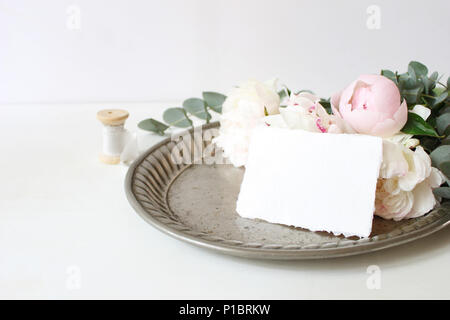 Feminine Hochzeit oder Geburtstag Tabelle Komposition mit floralen Bouquet. Weiß und rosa Pfingstrosen Blumen und Eukalyptus Niederlassungen auf alten Vintage Silbertablett, Handwerk Karte und Seidenband. Stockfoto