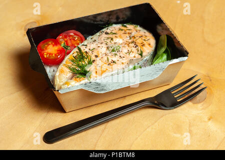 Gegrillte Forelle mit Reis und Kirschtomaten in schwarz Brotdose auf hölzernen Hintergrund Stockfoto