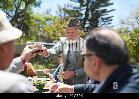 Älterer Mann in Anzug und Fliege toasten Freunde mit Wein bei Sunny Garden Party Stockfoto