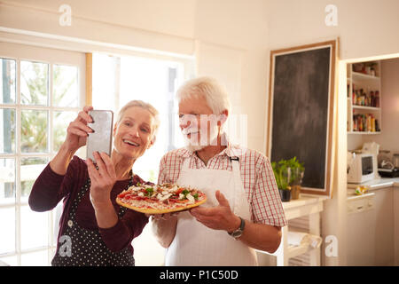 Lächelnd, zuversichtlich senior Paar unter selfie mit Pizza im Kochkurs Stockfoto