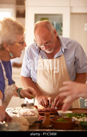 Ältere Menschen Salami schneiden im Kochkurs konzentriert Stockfoto