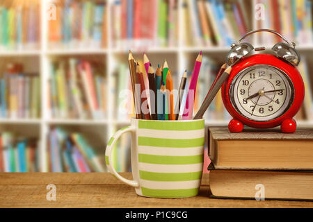 Das zusammengesetzte Bild der Bücher mit Wecker von Buntstifte in der Tasse auf dem Tisch Stockfoto