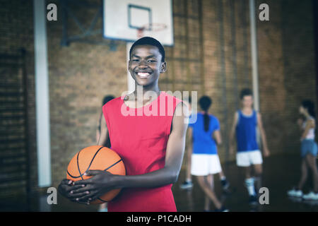 Lächelnd school boy Holding ein Basketball während Mannschaft spielen im Hintergrund Stockfoto