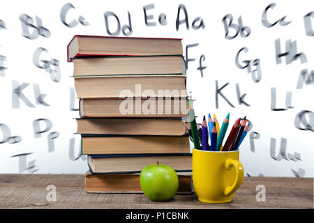 Stapel von Büchern Buntstifte in Tasse und Apple auf Tisch Stockfoto