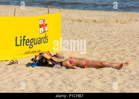 Boscombe, Bournemouth, Dorset, England, Großbritannien, 11.. Juni 2018, Wetter: Frau in einem Bikini, Sonnenbaden am Strand mit einem Hut über ihrem Gesicht. Stockfoto