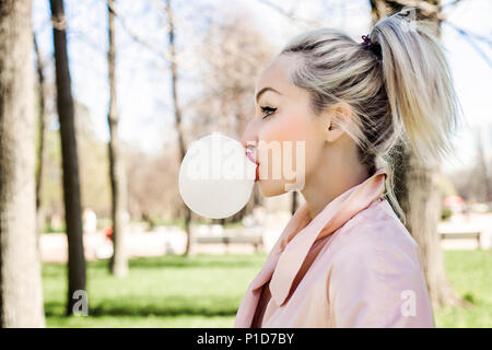 Junge Frau blasen Blase mit Kaugummi und Walking im Park im Freien, Lifestyle portrait Stockfoto