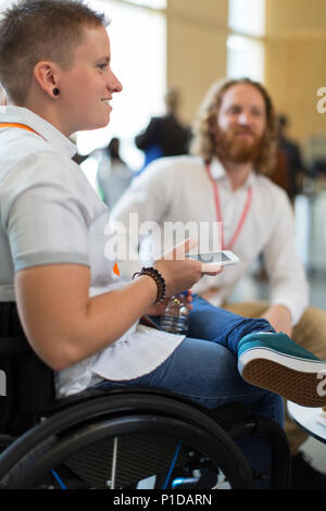 Frau im Rollstuhl mit smart phone bei der Konferenz Stockfoto