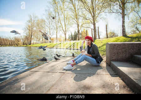 Glückliche Frau im Freien. Stilvolle blonde Frau in einem roten Barett, der Vogel ihr Feed Stockfoto