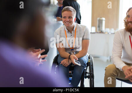 Lächelnde Frau im Rollstuhl im Gespräch mit Kollegen in der Konferenz Stockfoto