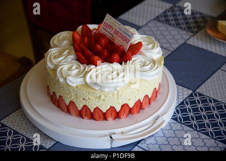 Geburtstag Kuchen: eine Erdbeere Geburtstag Kuchen mit einem mehrsprachigen Karte sagt 'Happy Birthday' Stockfoto