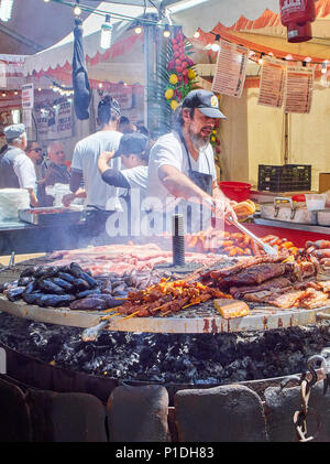 Madrid, Spanien - 15. Mai 2018. Hispanic Koch, Würstchen, Schweinerippchen und andere Fleisch auf einem Holzkohle Grill in einem Stall eines Street Food Fair. Stockfoto