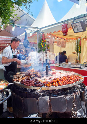 Madrid, Spanien - 15. Mai 2018. Hispanic Koch, Würstchen, Schweinerippchen und andere Fleisch auf einem Holzkohle Grill in einem Stall eines Street Food Fair. Stockfoto