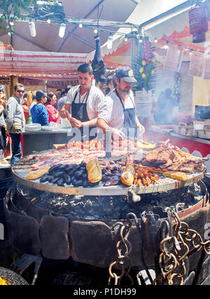 Madrid, Spanien - 15. Mai 2018. Hispanic Köche kochen Würstchen, Schweinerippchen und andere Fleisch auf einem Holzkohle Grill in einem Stall eines Street Food Fair. Stockfoto