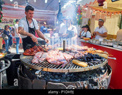 Madrid, Spanien - 15. Mai 2018. Hispanic Koch, Würstchen, Schweinerippchen und andere Fleisch auf einem Holzkohle Grill in einem Stall eines Street Food Fair. Stockfoto