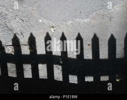 Schwarze Schatten von einem niedrigen Zaun auf einem grauen Licht Asphalt. Stockfoto