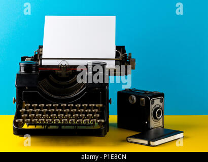 Vintage Schreibmaschine mit der leeren Blatt Papier, Kamera und Notebook auf Gelb und Cyan Hintergrund Stockfoto