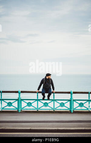 Touristische sitzt auf einem Geländer an der Küste, Strand von Brighton, Brighton, England Stockfoto