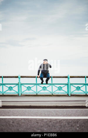 Touristische sitzt auf einem Geländer an der Küste, Strand von Brighton, Brighton, England Stockfoto