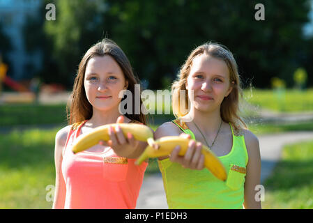 Zwei Freundinnen. Sommer in der Natur. Gerne erweitert eine Hand in die Hände der Banane. Gesunde Lebensweise. Die richtige Ernährung von Kindern. Nützliche Obst für Schulkinder. Stockfoto