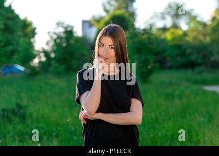 Die brünette Mädchen ist europäisch. Im Sommer im Park an der frischen Luft. Mit einer Hand hält er seine Lippen. Er sieht sie genau auf den Rahmen. Stellt geistig. Gefühle von Selbstvertrauen. Stockfoto