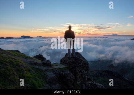 Denn der Mensch sieht auf Roque Bentayga und Teide über den Wolken bei Sonnenuntergang, Gran Canaria, Kanarische Inseln, Spanien Stockfoto