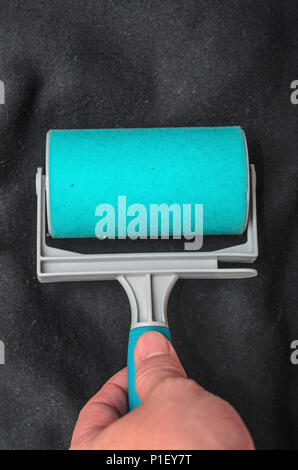 Mit der klebrigen Fussel Roller auf schwarzem Stoff Staub, Fell zu entfernen, Haare der Shirt. Reinigung Textilien mit einem Abwaschbaren blau klebrige Walze. Stockfoto