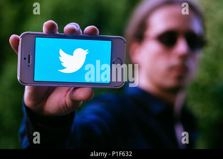 Nahaufnahme des ernsten jungen Mann mit weißen iPhone mit Twitter Logo auf dem Bildschirm Stockfoto