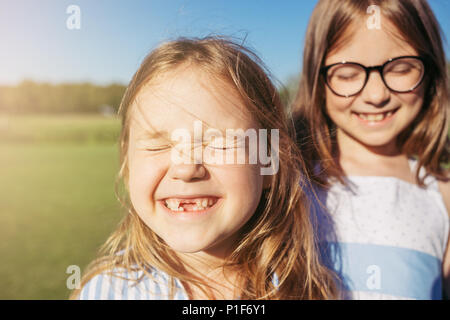 Zwei fröhliche Mädchen umarmen und schlossen ihre Augen vor der Sonne. Aufrichtiger Emotion. Mädchen ohne vorderen Zähne. Stockfoto