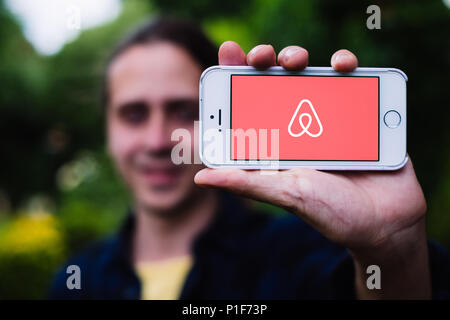 Nahaufnahme der junge Mann mit weißen iPhone mit AIRBNB Logo auf dem Bildschirm Stockfoto
